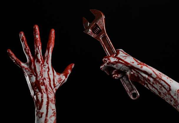 Halloween theme: bloody hand holding a big wrench on a black background - Foto, Imagen