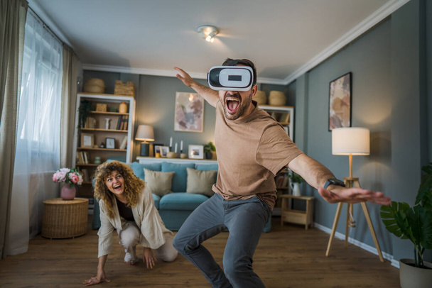 férfi érett felnőtt kaukázusi férfi férj feleségével vagy barátnőjével pár otthon élvezni a virtuális valóság VR headset googles a fejen jó szórakozást modern technológia szabadidő koncepció másolás tér - Fotó, kép