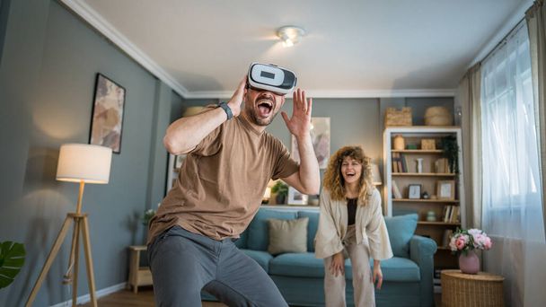 man mature adult caucasian male husband with his wife or girlfriend couple at home enjoy virtual reality VR headset with googles on the head have fun modern technology leisure concept copy space - Foto, imagen