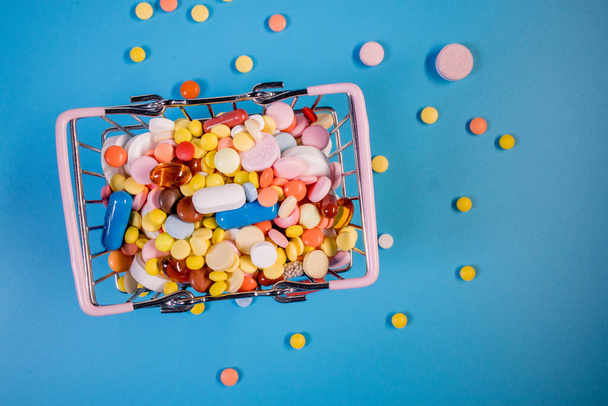 Various capsules, pills and medicines in a shopping cart on a blue background. Health care, treatment. The concept of buying pills and buying medicine. - Foto, immagini