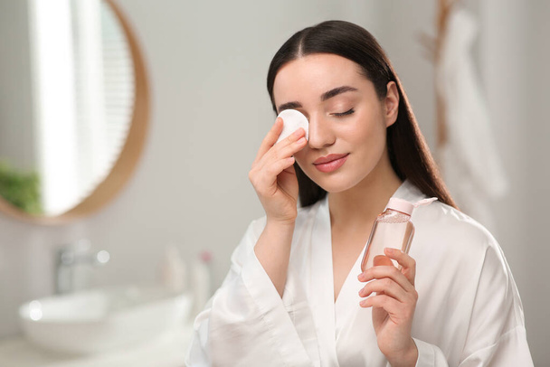 Beautiful woman removing makeup with cotton pad indoors - Photo, Image