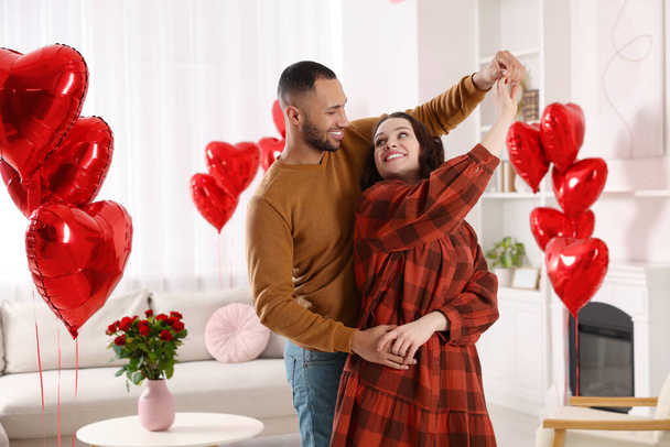 Lovely couple dancing in room decorated with heart shaped air balloons. Valentine's day celebration - Fotografie, Obrázek