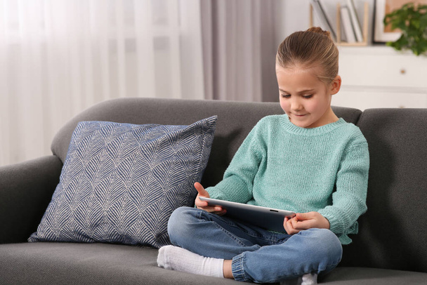 Little girl using tablet on sofa at home. Internet addiction - Fotografie, Obrázek