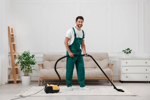 Dry cleaner's employee hoovering carpet with vacuum cleaner in room - Fotó, kép