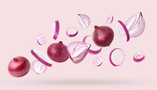 Whole and cut fresh red onions falling on light pink background - Фото, изображение