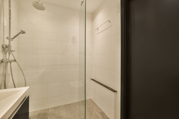ванна кімната зі скляними дверима для душу і раковина в кутку поруч з нею велике дзеркало на стіні
 - Фото, зображення