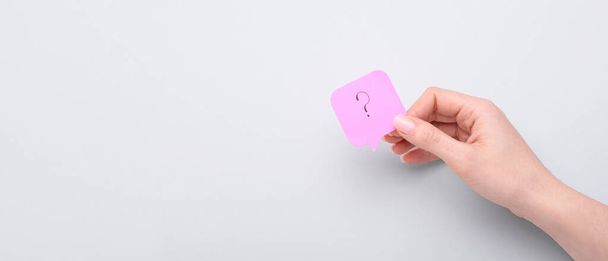 Female hand holding sticky paper with question mark on light background with space for text - Photo, Image