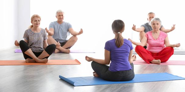 Senior people with young trainer doing exercises in gym - Photo, Image