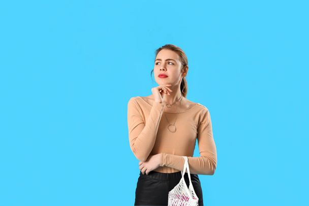 Mujer joven pensativa con bolsa de hilo sobre fondo azul - Foto, Imagen