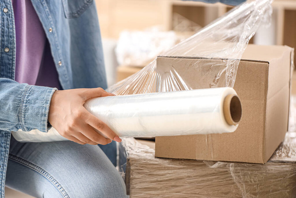 Young woman wrapping cardboard box with stretch film at home on moving day, closeup - Photo, Image