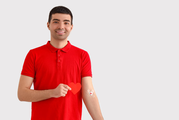 Donante de sangre joven con parches médicos aplicados y corazón de papel sobre fondo claro - Foto, imagen