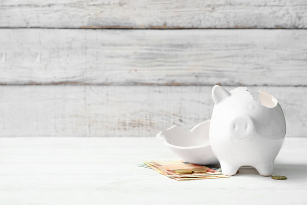 Broken piggy bank with money on white wooden background. Concept of bankruptcy - Foto, Imagem