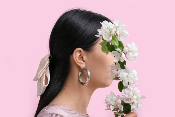 Profilo di bella giovane donna che indossa gioielli alla moda con fiore vicino alla parete rosa - Foto, immagini