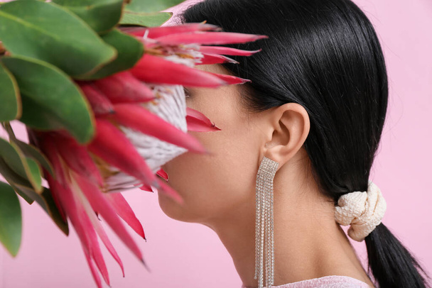 Perfil da bela jovem mulher vestindo brincos elegantes com flor de protea perto da parede rosa - Foto, Imagem