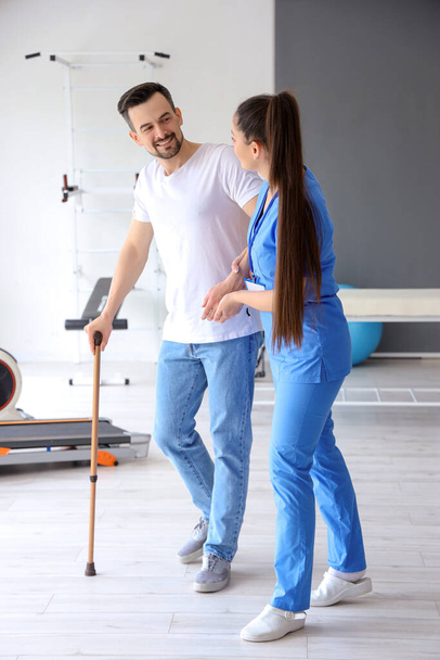 Physiothérapeute féminine aidant jeune homme avec bâton de marche dans le centre de réadaptation - Photo, image