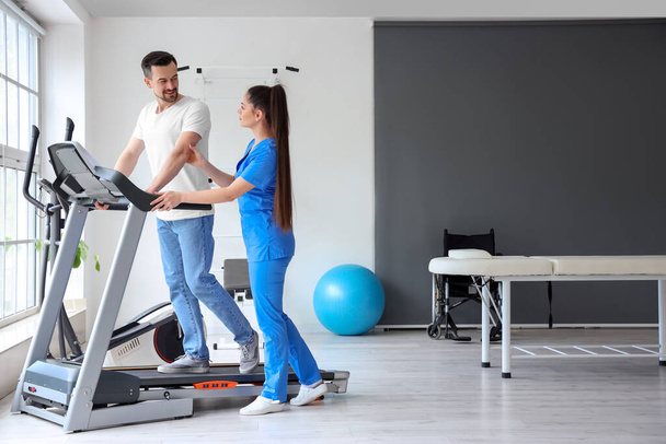 Fisioterapeuta femenina trabajando con un joven en una cinta de correr en un centro de rehabilitación - Foto, imagen