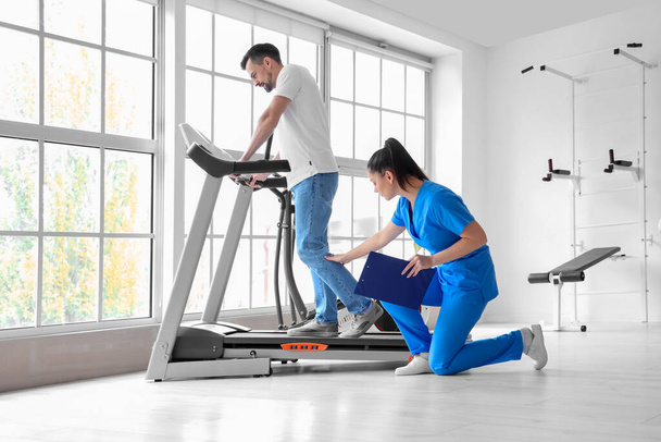Female physiotherapist working with young man on treadmill in rehabilitation center - Фото, зображення
