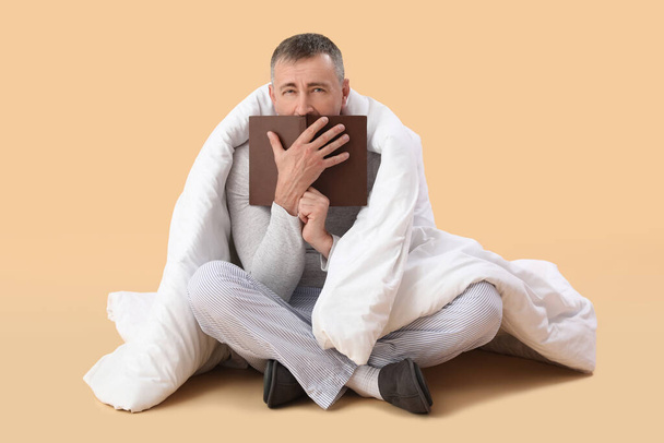 Mature man with soft blanket reading book on beige background - Photo, image