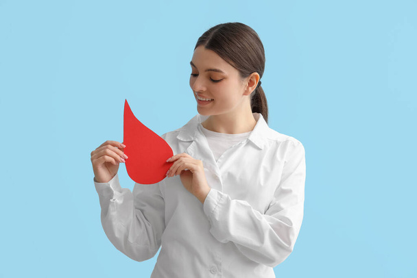 Female doctor with paper blood drop on blue background - Photo, Image
