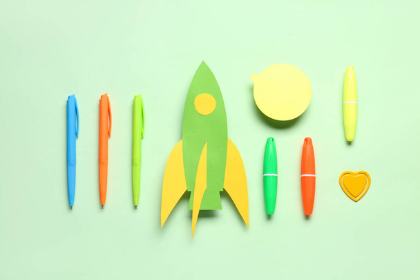 Paper rocket with different stationery and speech bubble on green background - 写真・画像