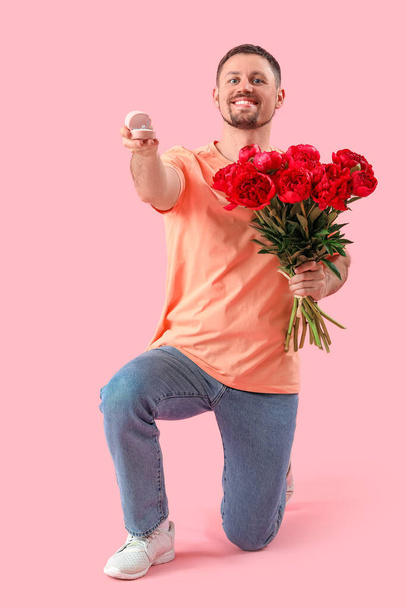 Young man with engagement ring and flowers on pink background - Foto, Imagen