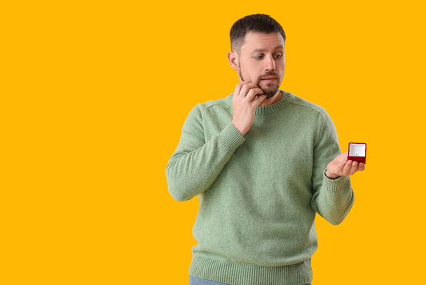 Worried young man with engagement ring on yellow background - Fotó, kép