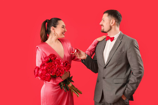 Young man proposing to his girlfriend with flowers on red background - Photo, Image