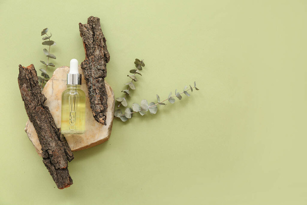 Composition with bottle of essential oil, tree bark, stone and eucalyptus branches on color background - Foto, immagini