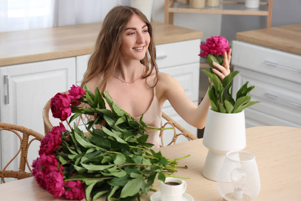Όμορφη νεαρή γυναίκα με μπουκέτο από λουλούδια παιώνιας στην κουζίνα - Φωτογραφία, εικόνα