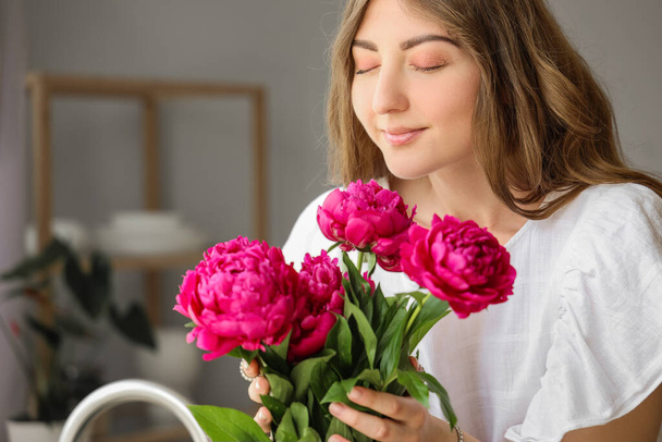Красива молода жінка з букетом півонійних квітів на кухні
 - Фото, зображення