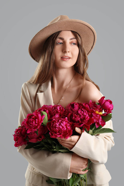 Schöne junge Frau mit Strauß von Pfingstrosen Blumen auf grauem Hintergrund - Foto, Bild