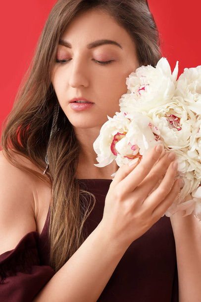 Beautiful young woman with bouquet of peony flowers on red background - Photo, Image