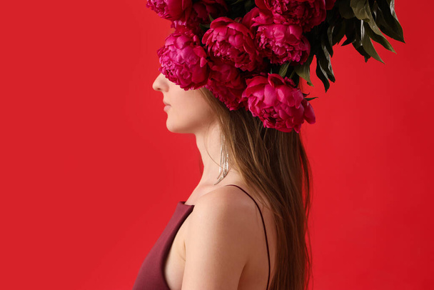 Beautiful young woman with bouquet of peony flowers on red background - Φωτογραφία, εικόνα