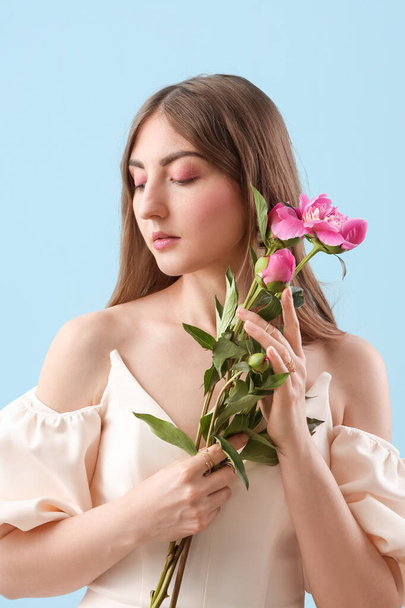 Mooie jonge vrouw met pioenroos bloemen op blauwe achtergrond - Foto, afbeelding