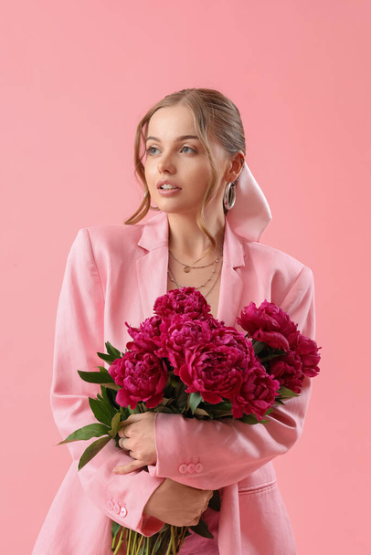 Beautiful young woman with bouquet of peony flowers on pink background - Foto, afbeelding