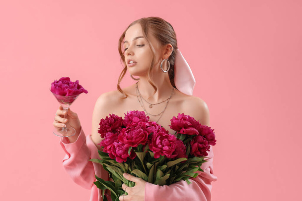 Schöne junge Frau mit einem Strauß von Pfingstrosenblumen auf rosa Hintergrund - Foto, Bild