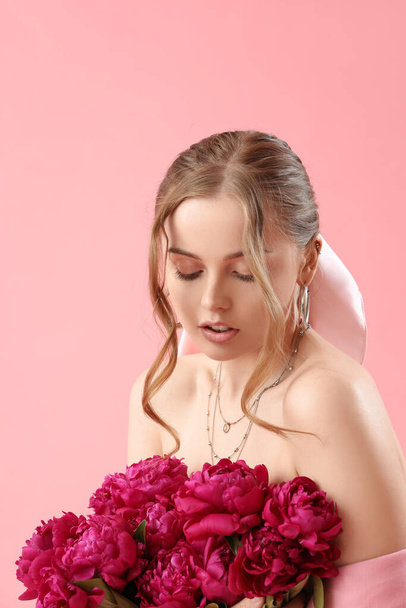 ピンクの背景に牡丹の花の花束を持つ美しい若い女性 - 写真・画像