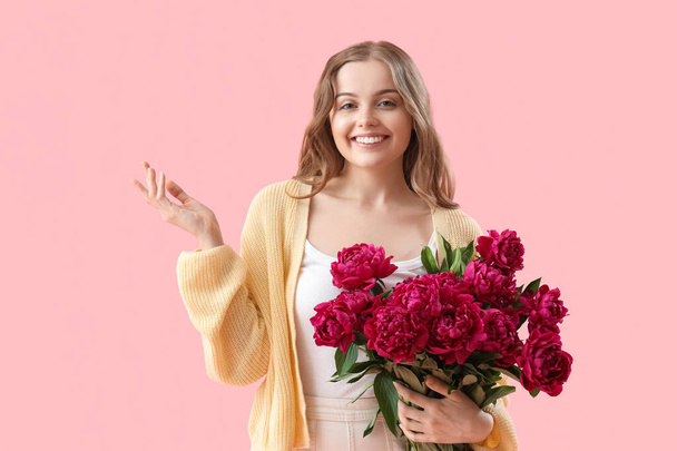 Όμορφη νεαρή γυναίκα με μπουκέτο από λουλούδια παιώνιος σε ροζ φόντο - Φωτογραφία, εικόνα