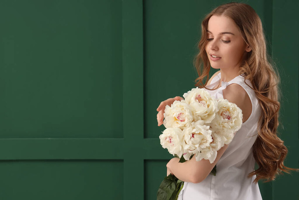 Beautiful young woman with bouquet of peony flowers on green background - Photo, Image