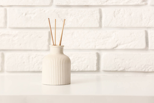 Bottle of reed diffuser on table near light brick wall in room - Photo, image