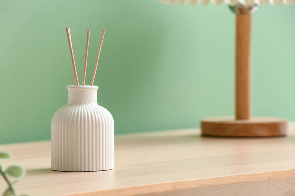Bottle of reed diffuser on table near color wall in room, closeup - 写真・画像