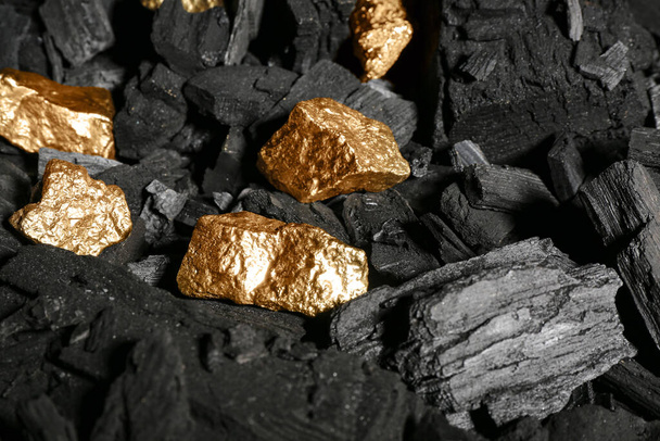 Gouden nuggets op zwarte houtskool, close-up - Foto, afbeelding