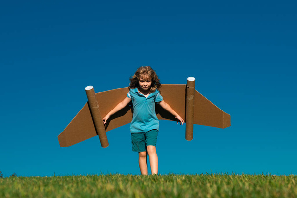 Kid with toy jetpack outdoor. Child run with paper wings against blue sky. Kid dreams of future. Kid pilot dreaming. Dream concept. Blonde cute daydreamer child dream on fly. Dreams and imagination - Photo, Image