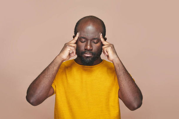 Afroameričan uvažuje o nové myšlence držet hlavu s rukama opřenýma o hnědé pozadí - Fotografie, Obrázek