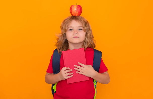 Apple on head, idea concept. Child from elementary school with book and apple isolated on yellow background. Little student, clever nerd pupil ready to study - Foto, immagini
