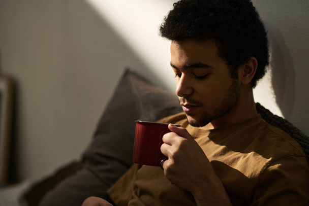 Nahaufnahme eines jungen Mannes, der in seiner Freizeit heißen Tee aus einer Tasse in seinem Schlafzimmer trinkt - Foto, Bild