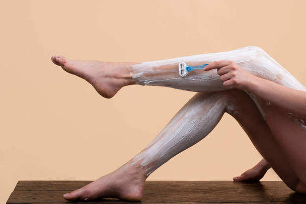 Sexy woman shaving legs. Hygiene skin body care concept. Hair removal. Woman shaving legs with razor blade. Shaving legs with razor. Hairy legs, body care. Shaving foam cream, razor and shaved hair - Foto, Bild