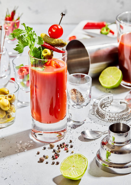 Preparation of bloody mary cocktail in bar with utensils and lime,pepper,olives on light board.Hard light - 写真・画像