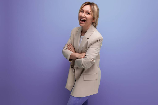 положительная 30-летняя женщина в пиджаке с светлыми волосами на фоне студии с копировальным пространством. - Фото, изображение