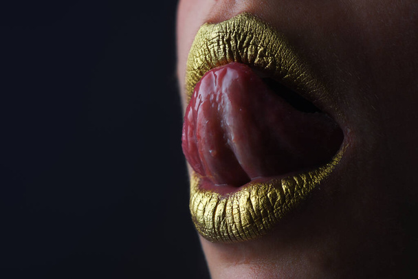 Sensual tongue licking lips. Sensual mouth. Symbol of kiss from golden lipstick. Glamour luxury gold mouth. Gold paint on lips. Golden lips, sensual woman mouth. Metallic body. Gold concept - Photo, image